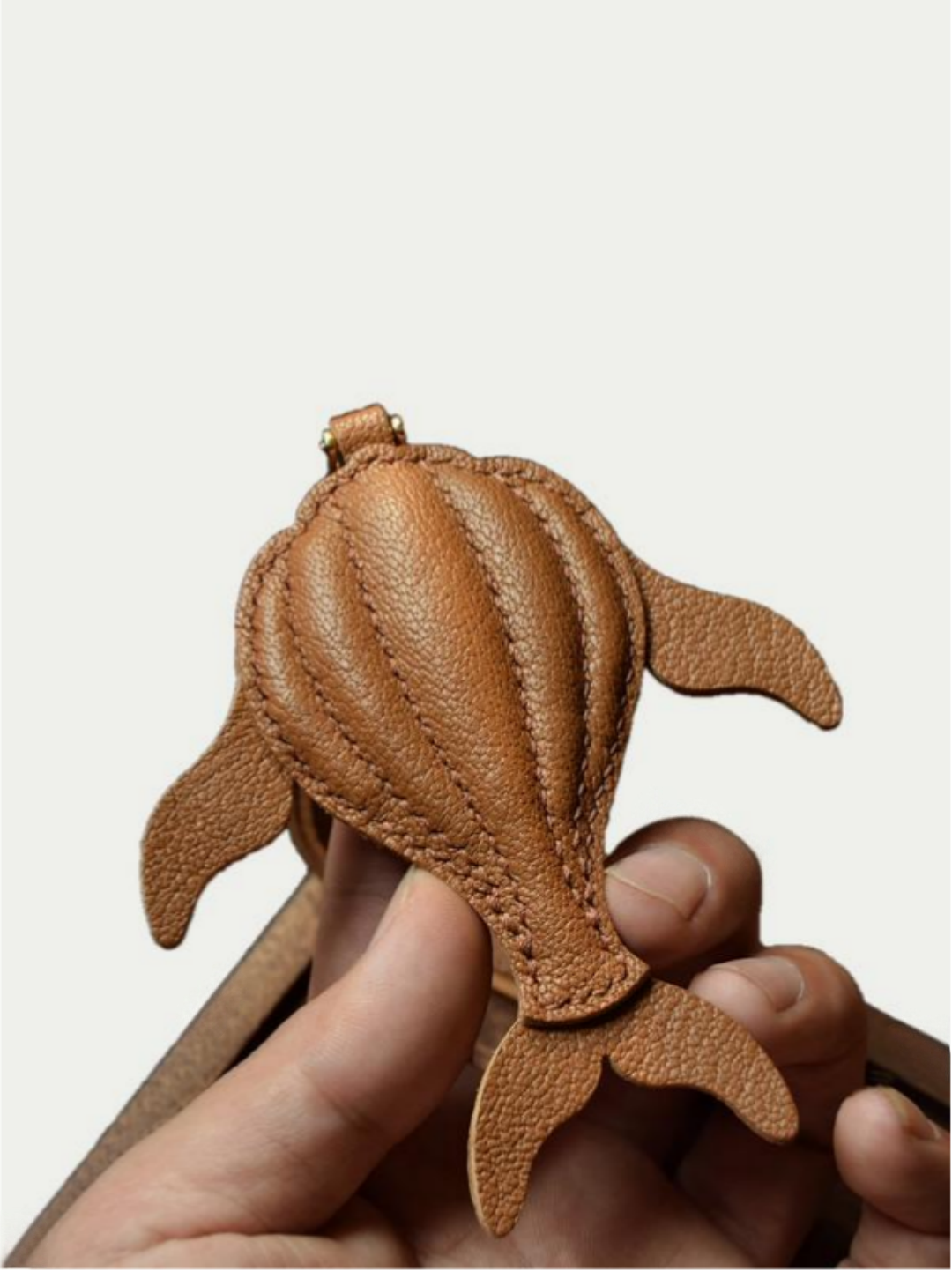 Ocean brown whale leather charm hanging from a cream handbag

